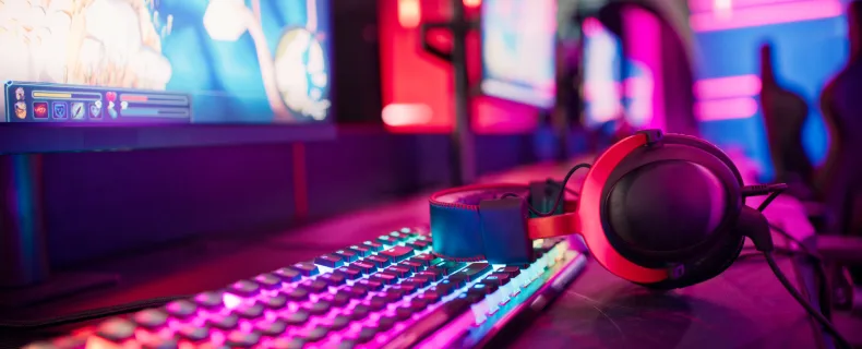 gaming headphones sitting on keyboard on a desk with half of a monitor entertainment