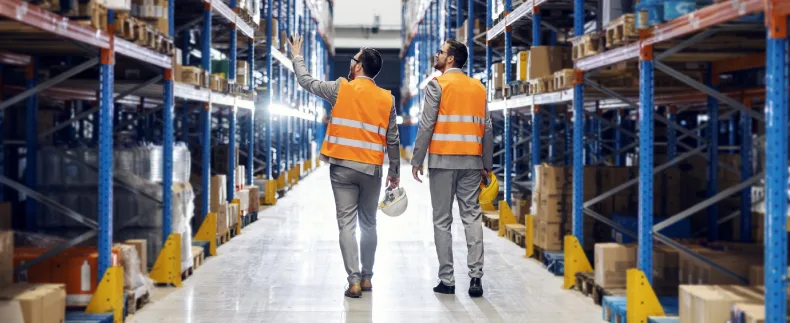 two men walking through a warehouse point out boxes