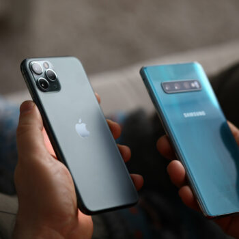 Man holding an Apple phone in one hand and a Samsung phone in another hand.