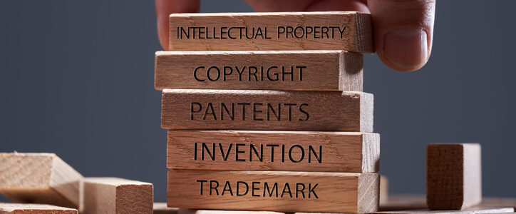 man adding a block showing the words Intellectual property on top of other wooden block with text copyright, patents, invention,and trademark