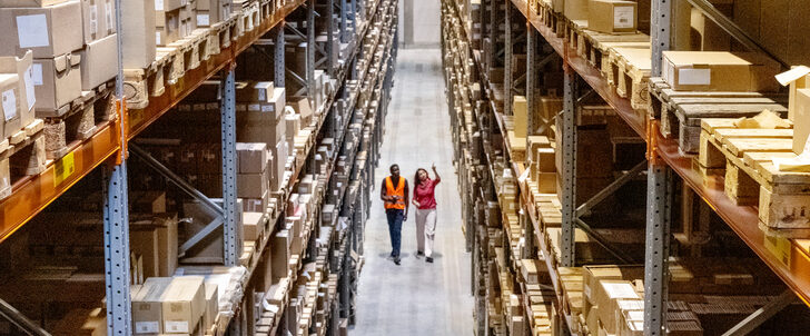 High angle view of a warehouse manager walking with foremen checking stock on racks.