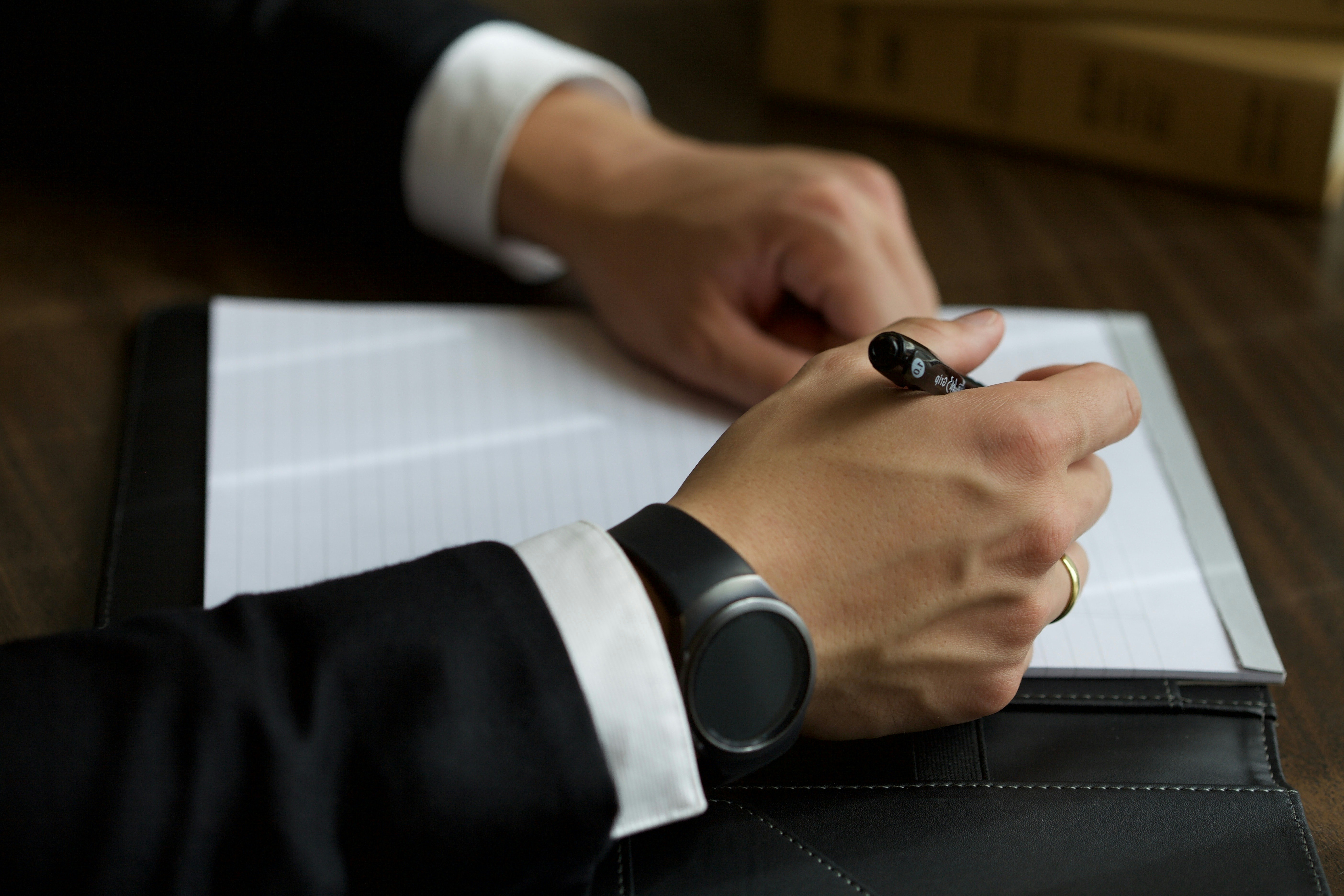 A man's hands, wearing a business suit and a watch, hold a pen over a blank document.