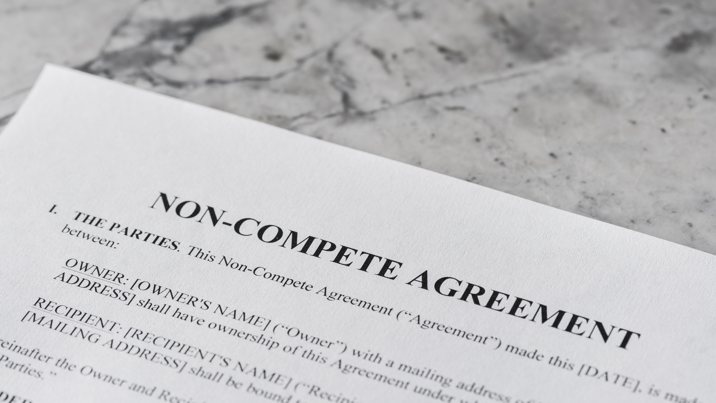 A close-up of a "NON-COMPETE AGREEMENT" document on a marble surface.