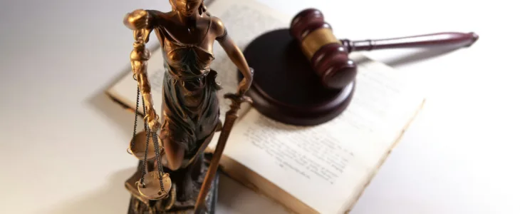 A law book with a gavel on it and a statue of Lady Justice