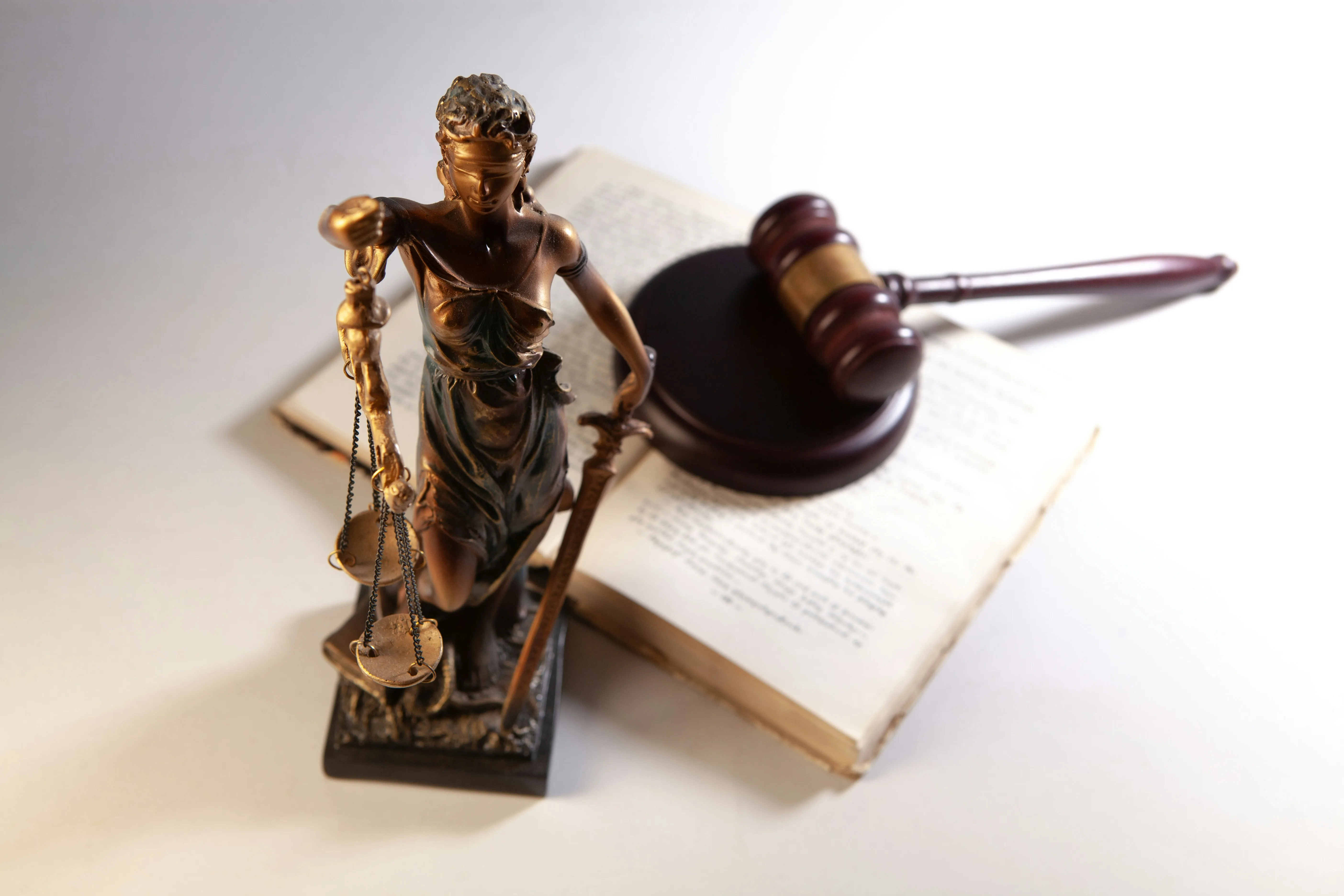 A law book with a gavel on it and a statue of Lady Justice