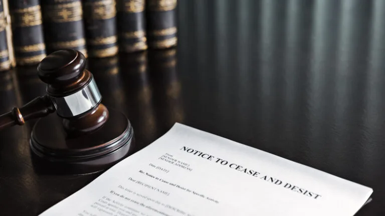A legal notice titled "NOTICE TO CEASE AND DESIST" is on a dark desk next to a gavel and several books.