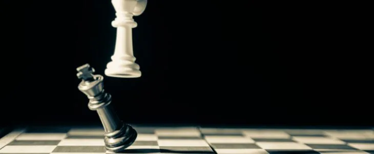 A chess king being toppled by a white king piece.